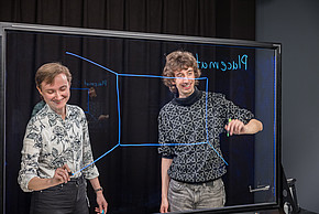 Zwei Personen stehen vor digitalem Board und schreiben darauf