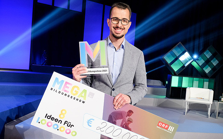 Translate to English: Tarik Mete nahm den Preis in der Finalshow „8 Ideen für eine Million – Die MEGA-Bildungsshow“ auf ORF III für das Projekt YELP entgegen. ©MEGA Bildungsstiftung/ORF