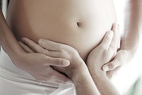 Hände umfassen den Bauch einer Schwangeren