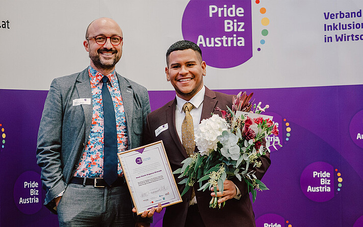 Masterabsolvent Josua Steele bekommt den Pride Biz Pride Biz Austria Best Paper Award 2022 verliehen. (©Glitter & Confetti)