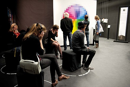 Besucher einer Ausstellung über die Zeit sitzen mit Kopfhörern, im Hintergrund betrachten Besucher Ausstellungsobjekte