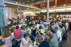 Personen sitzen an Tischen im Foyer der FH und unterhalten sich