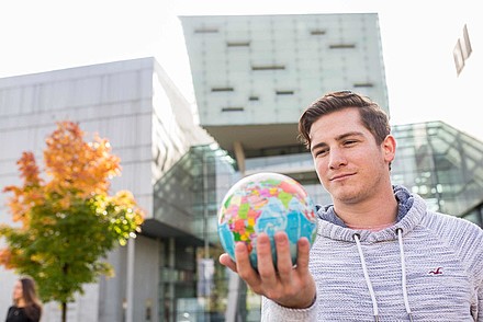 Student mit Weltkugel in der Hand vor herbstlichen Eingang Campus Urstein