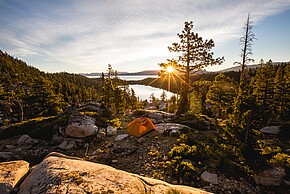 Beautiful shot of an orange tent on rocky mountain surrounded by trees during sunset