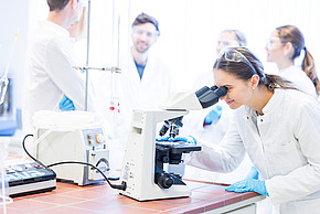 Studentin die in ein Mikroskop schaut im Labor am Campus Kuchl