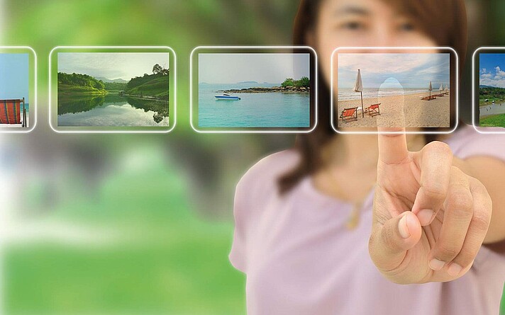 Junge Frau zeigt mit Finger auf einen transparenten Screen mit Urlaubsfotos
