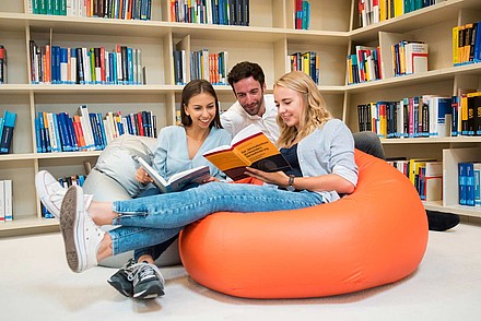 Drei Studierende auf bequemen Sitzsäcken in der Bibliothek und Büchern