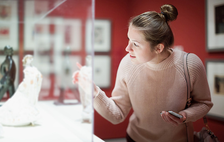 Young woman visitor using phone in museum