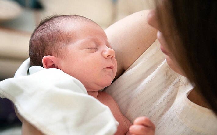 Hebamme hält ein Neugeborenes im Arm.
