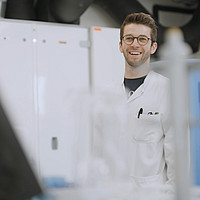 Eine Person steht hinter Labor-Utensilien im weißen Kittel