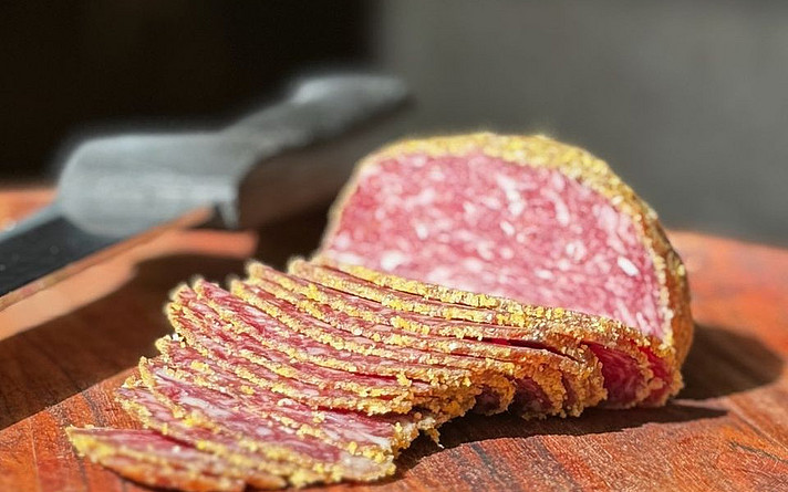 ein holzbrett mit aufgeschnittener italienischer salami, im hintergrund liegt ein messer