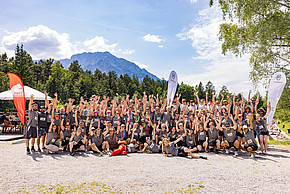 Große Personengruppe posiert vor Berg- und Waldhintergrund