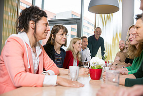 Personengruppe sitzt um einen Tisch und unterhält sich