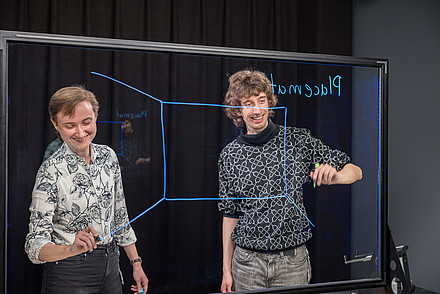 Zwei Personen stehen vor digitalem Board und schreiben darauf