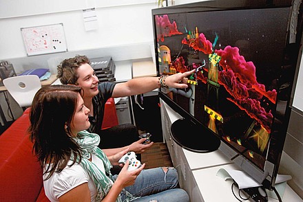 Zwei Studierende sitzen vor großem Screen mit Computeranimationen